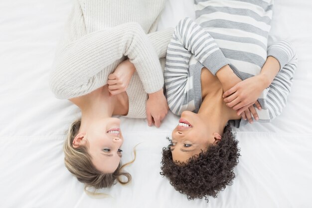 Two casual young female friends lying in bed