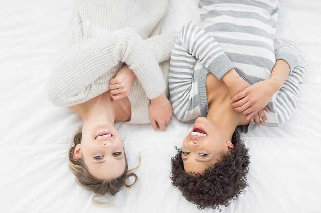 Photo two casual young female friends lying in bed