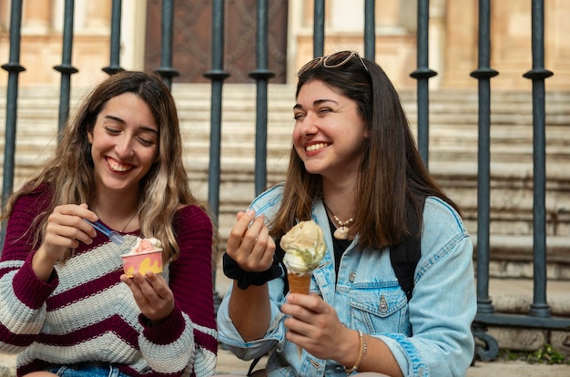 Foto due ragazze caucasiche sedute su una scala che mangiano gelato e chiacchierano con le facce sorridenti