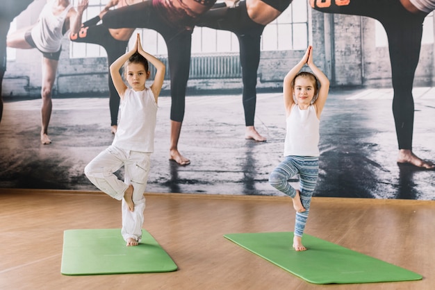 Foto una bambina di due caucasici che si esercita sulla stuoia di yoga sopra superficie di legno