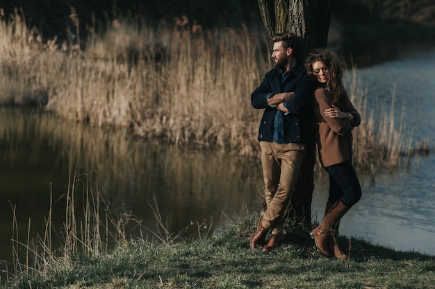 사진 두 백인 연인은 호수 옆 나무 근처에 서 있습니다. 수염 난 남자와 사랑에 곱슬 여자. 발렌타인 데이.