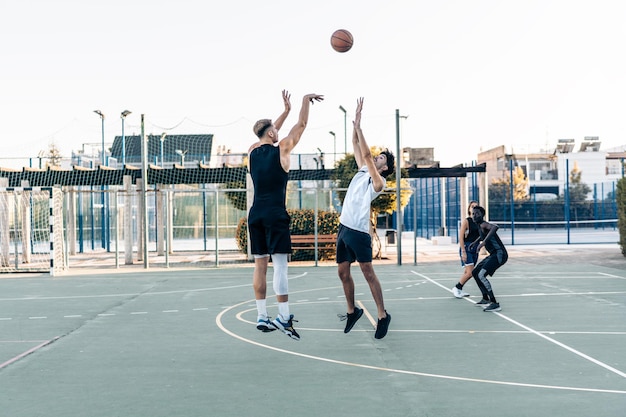 Two caucasian men jumping while playing basketball between friends in an urban outdoor court