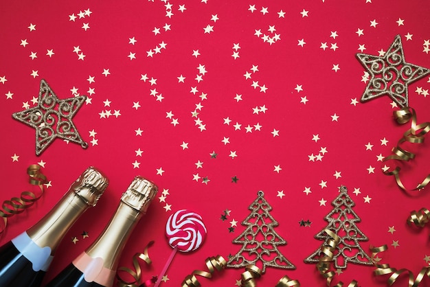 赤い背景のクリスマスに2つのシャンパンボトルクリスマスオーナメントキャンディーと紙吹雪の星