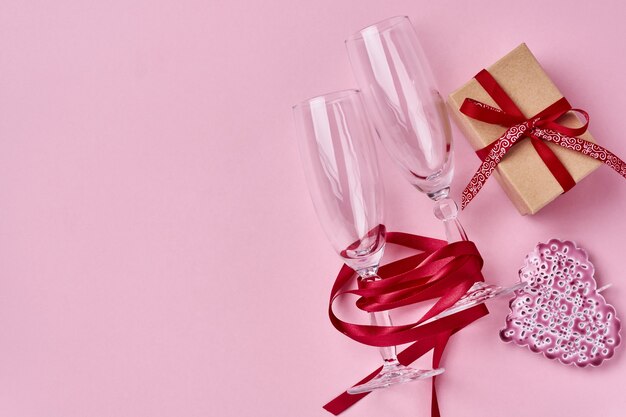 Два бокала шампанского, подарочная коробка, красивая саржа и красная лента на сверкающем розовом фоне
