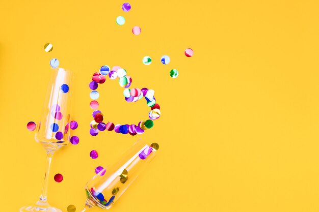 Two champagne glasses and confetti on yellow background