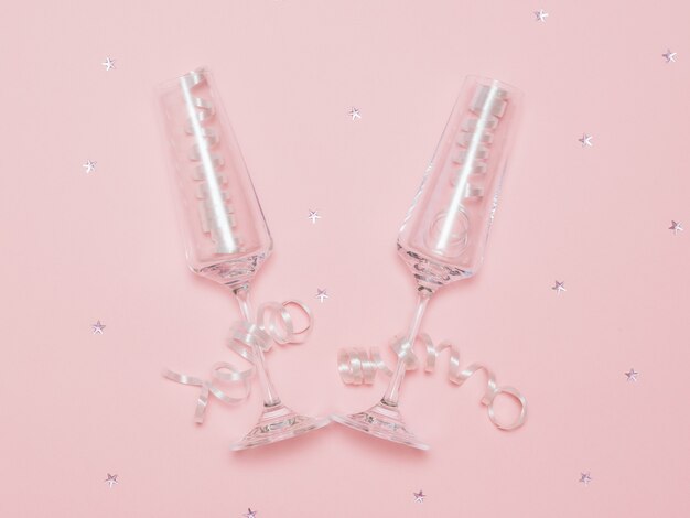 Two champagne glasses with streamers on a pink background with scattered sequins. Festive background with champagne glasses.