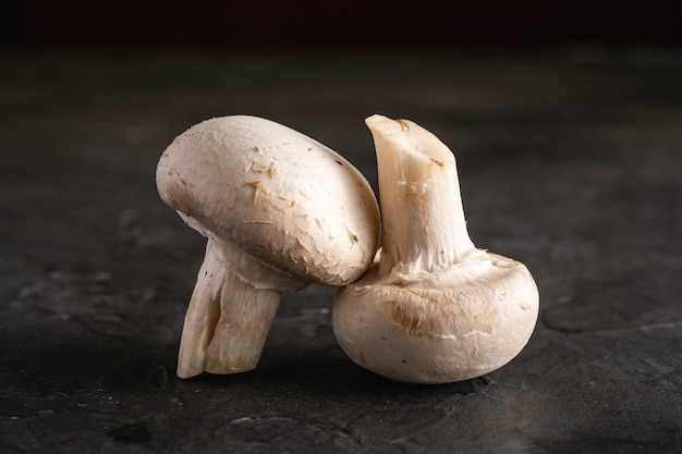 Two champignon mushrooms healthy food on dark black textured background, macro