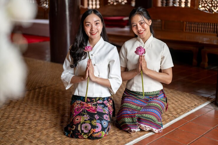 Photo 伝統的な服を着た2人の魅力的なアジア人女性が祈りの姿勢で蓮を手にして寺院に座っています