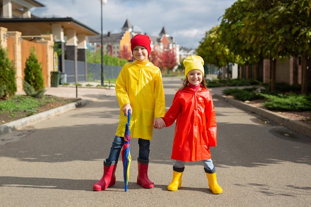 Two charming children a boy and a girl in waterproof raincoats and rubber boots with an umbrella