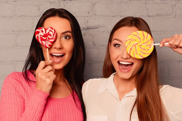 Foto due affascinanti ragazze felici che nascondono i loro occhi con lecca-lecca e sorridenti