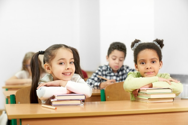 Two charming students sitting at table in school and posing