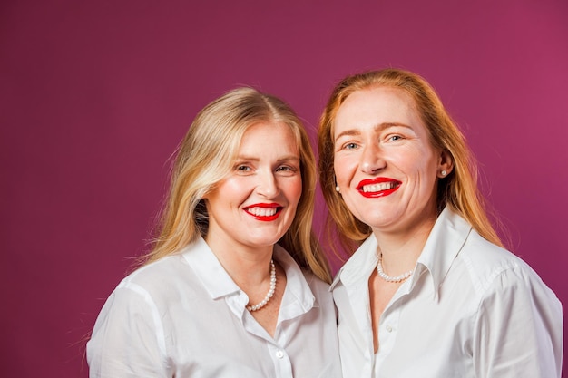 Two charming women young looking mother and adult daughter both wearing white shirts and red lipstick Natural beauty concept Studio with purple background