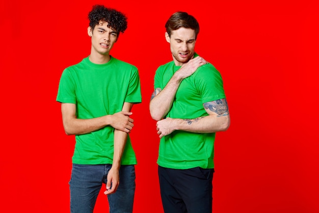 Photo two cheerful friends in green tshirts communicating emotions red background high quality photo