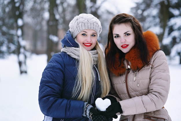 Two cheerful girlfriends holding a snowy heart