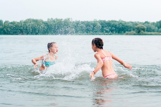 두 명의 쾌활한 소녀가 강에서 서로 물을 튀깁니다. 지역 관광 여름 방학
