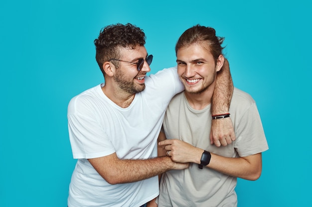 Two cheerful guys embracing each other isolated over blue wall