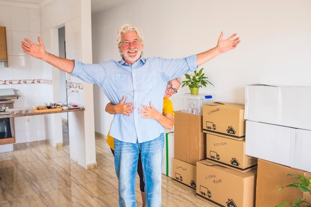 Two cheerful senior people happy of new home for new beginning\
like retired with moving boxes on the floor - bright light from\
window