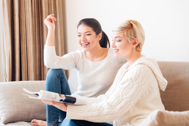 Two cheerful women reading magazine on the sofa at home