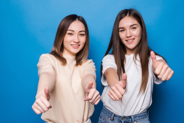 Two cheerful women thumbs up isolated on blue wall. People lifestyle concept. Mock up copy space. Showing thumbs up