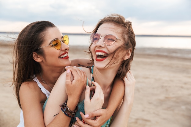 Two cheerful young girls friends spending good time at the beach, laughing