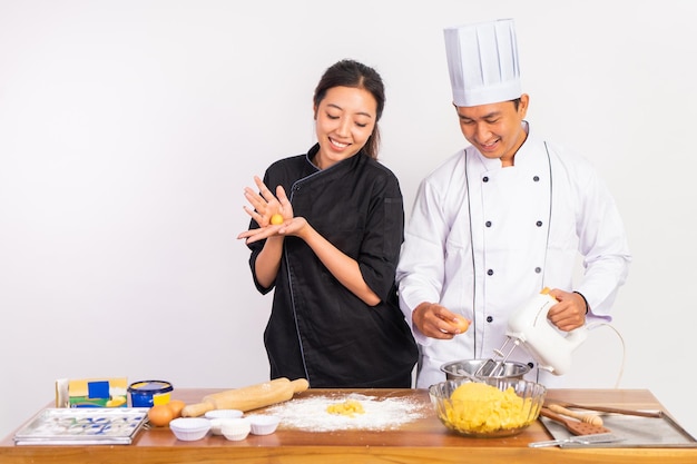 Two chefs working together making dough with mixer and whisk on table on isolated background