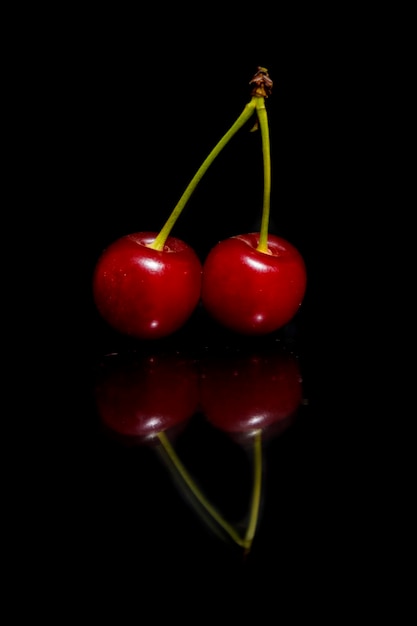 Photo two cherries on a black background with reflection