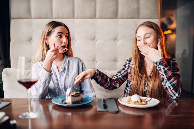 Photo two chicks drinks beverages and eats cakes in cafe