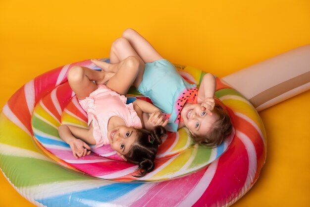 Two child girl in swimming suit lying having fun on colorful inflatable mattress lollipop.