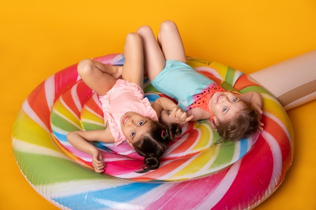 Two child girl in swimming suit lying having fun on colorful inflatable mattress lollipop.