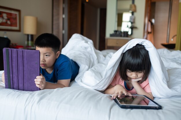 Двое детей пристрастились к планшету, азиатский ребенок смотрит мультфильм