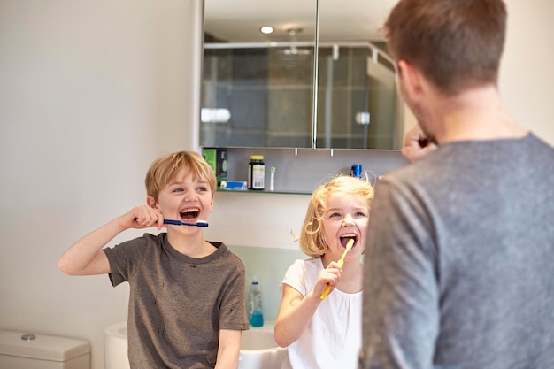 Photo two children and an adult man cleaning their teeth with toothbrushes in a bathroom