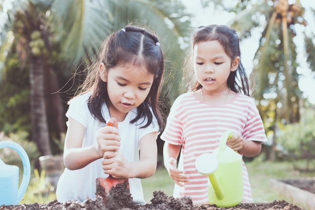 苗木を植えるための土壌を準備するために楽しい2人の子供のアジアの女の子若い木