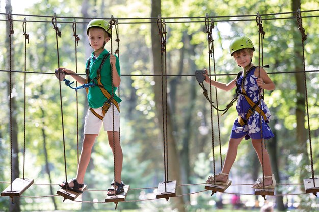 Two children, boy and girl in protective harness and safety helmets at climbing activity on rope way.