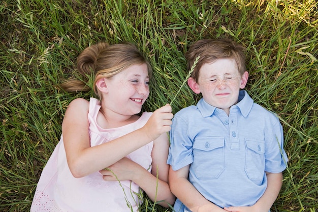 Photo two children brother and sister lying side by side on the grass