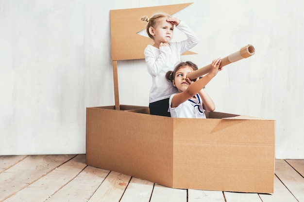 Two children little girls home in a cardboard ship play captains and sailors