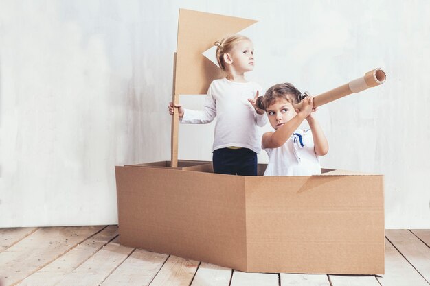 Two children little girls home in a cardboard ship play captains and sailors