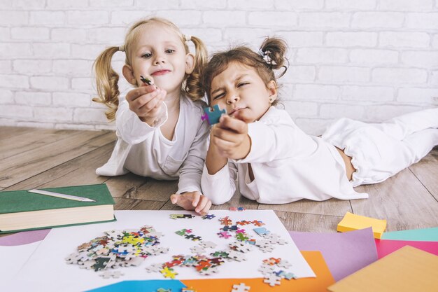 Due bambini, bambine in età prescolare mettono insieme il puzzle sul pavimento