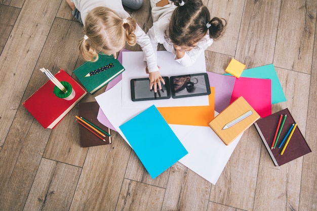 Two children, little girls of preschool age watching tablet at home on the floor