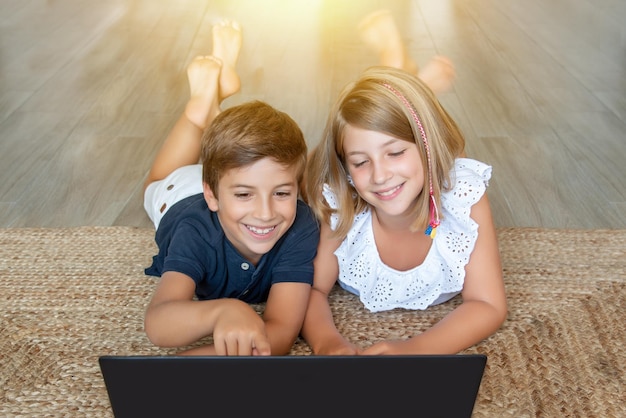 リビング ルームの床に横たわって、ラップトップ コンピューターで学習し、遊んでいる 2 人の子供