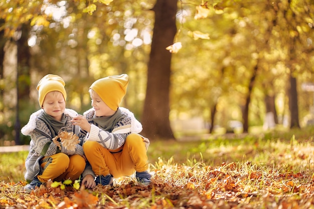 Foto due bambini giocano in autunno nel parco. due fratelli raccolgono le foglie cadute. copia spazio.