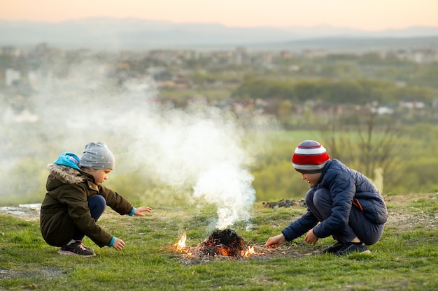 Two children playing with fire outdoors in cold weather.