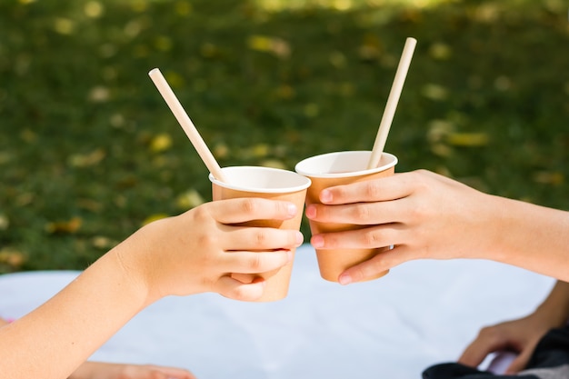 Le mani di due bambini tengono tazze e tubi ecologici con succo di mela durante un picnic nel parco. stoviglie usa e getta ecologiche