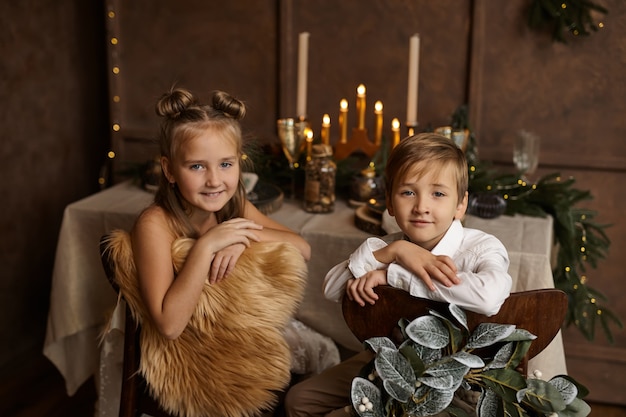 Two children sit on chairs near a festive table