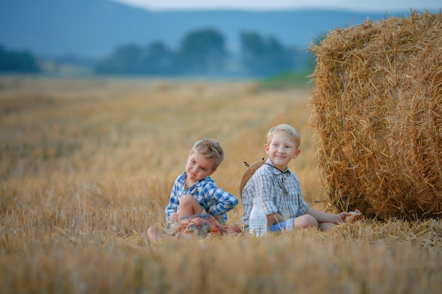 Two children sitting in a field of mown wheat near a pile of hay
