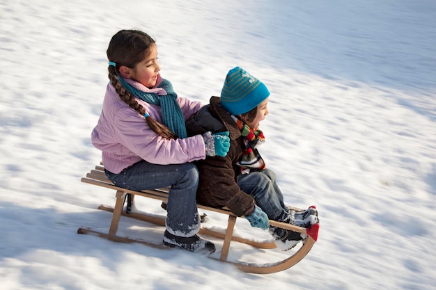 Two children on a sled having fun in the snow in wintertime