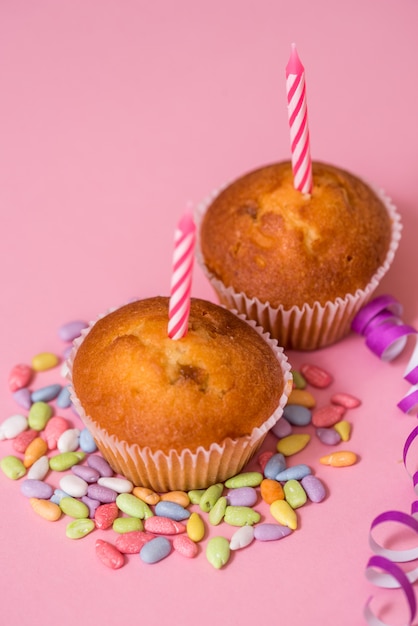 Due muffin al cioccolato, una candela di compleanno. festa per ragazze. caps e tinsel e dolci multicolori su uno sfondo rosa.