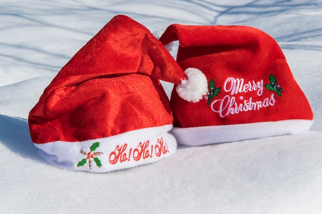 Two Christmas red hats on the white snow holiday celebration concept