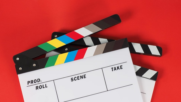 Две доски с хлопушкой или кинопластинка белого и радужного цвета на красном фоне.