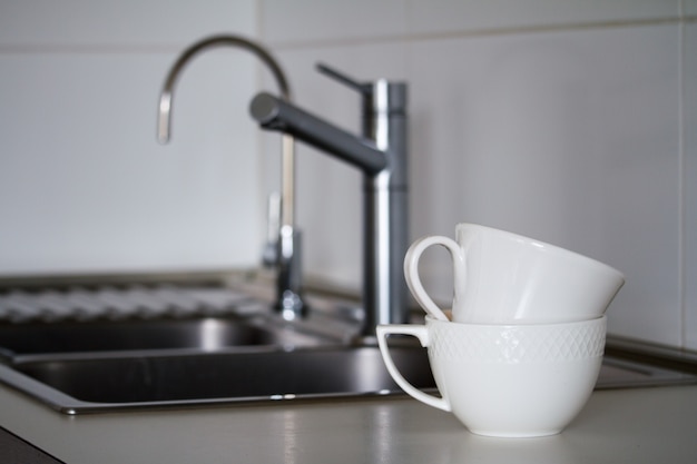 Two clean white tea cups near metal sink