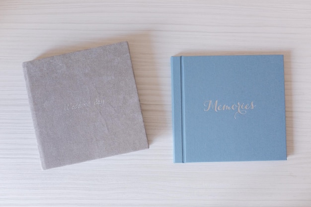 Two closed photobook on white wooden table Blue and grey wedding album with silver embossing